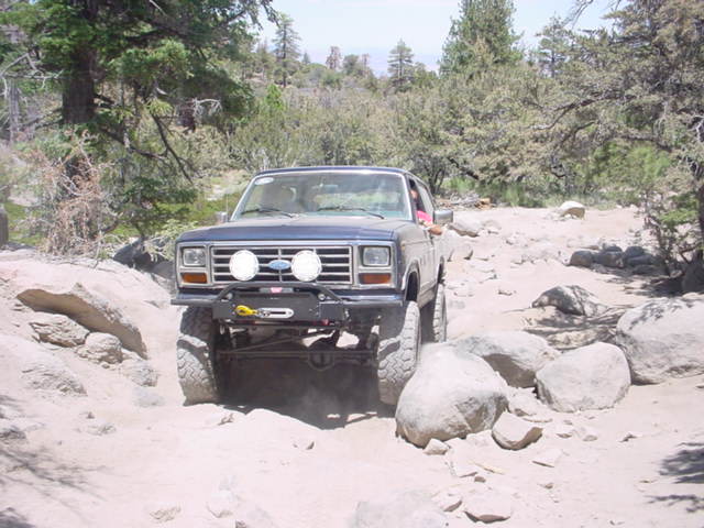 Blue lifted Ford Bronco crawling over rocks on a dusty mountain trail
