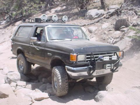 1988 Ford Bronco - This 1988 Ford Bronco navigates a challenging rocky trail, equipped with auxiliary lights and a protective brush guard.
