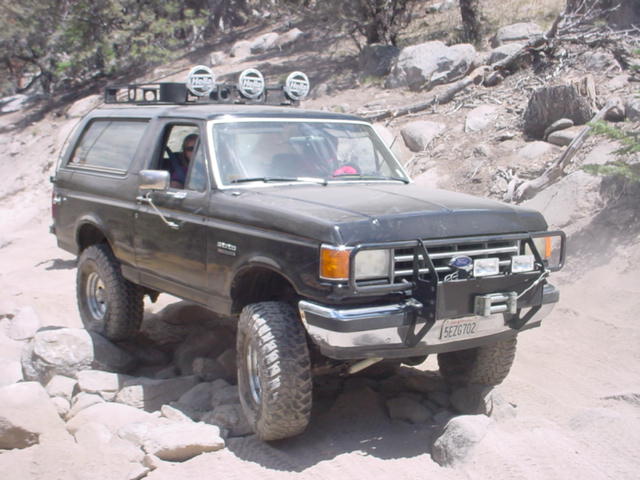 Black 1988 Ford Bronco with roof lights and brush guard on rocky terrain
