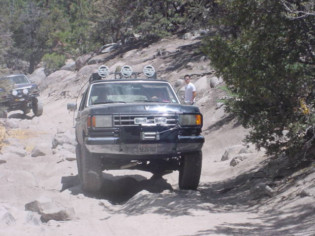 1988 Ford Bronco driving on a rocky off-road trail with another vehicle behind it