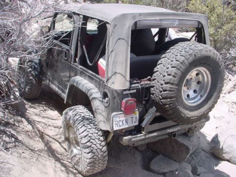 1988 Ford Bronco - This Jeep Wrangler TJ is navigating a rough, rocky off-road trail with its soft top deployed.