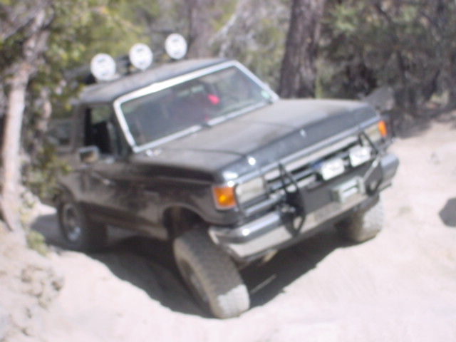 Dark SUV with off-road lights on roof, driving on a dirt path