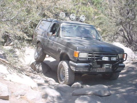 1988 Ford Bronco - This Ford Bronco is shown off-roading on a rocky trail with sparse vegetation.