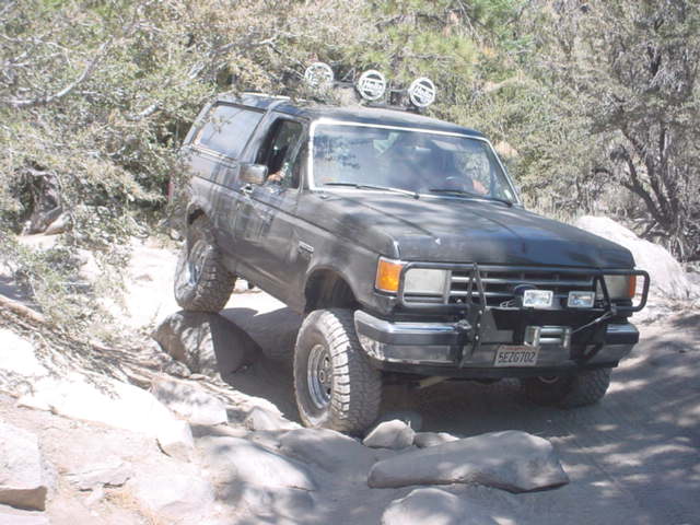 Black Ford Bronco navigating rocky terrain, has a winch and extra lights