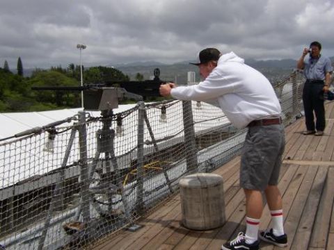 1989 Ford Bronco - A man aims a mounted machine gun on a wooden deck, with another person taking a photo in the background.