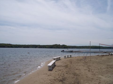 1990 Ford Bronco - A scenic view of a boat docked at a pier on a lake, with a sandy beach and benches in the foreground.
