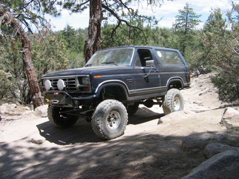 Dark blue lifted Ford Bronco with off-road tires on a rocky forest trail