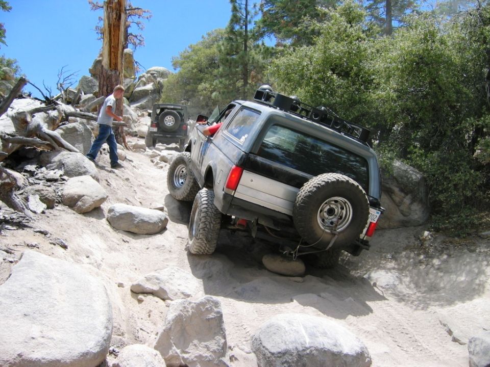 Silver and black Bronco climbing rocky off-road trail with Jeep ahead
