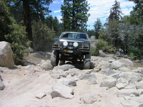 1985 Ford Bronco - This modified Ford Bronco is tackling a challenging off-road course filled with large rocks and uneven terrain.