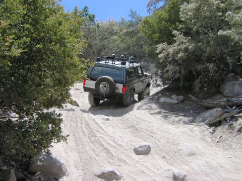 1985 Ford Bronco - Ford Bronco navigates a challenging off-road path surrounded by natural terrain.