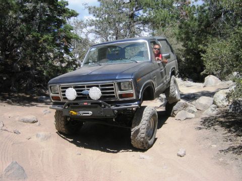 1985 Ford Bronco - This modified SUV is shown off-roading on a challenging rocky path.