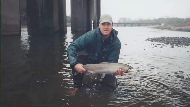 Man in waders holding a large fish in a river under a bridge