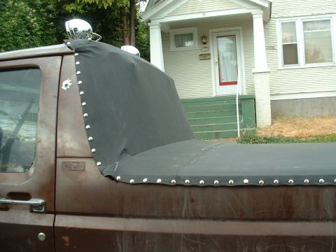 1982 Ford Bronco - A brown pickup truck with a custom black tonneau cover and spotlights is parked in front of a house.