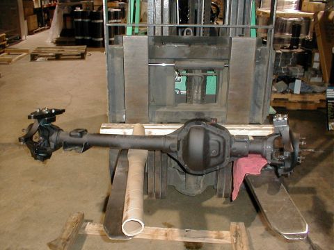 1983 Ford Bronco - A rear axle assembly is shown being moved by a forklift in a warehouse setting.
