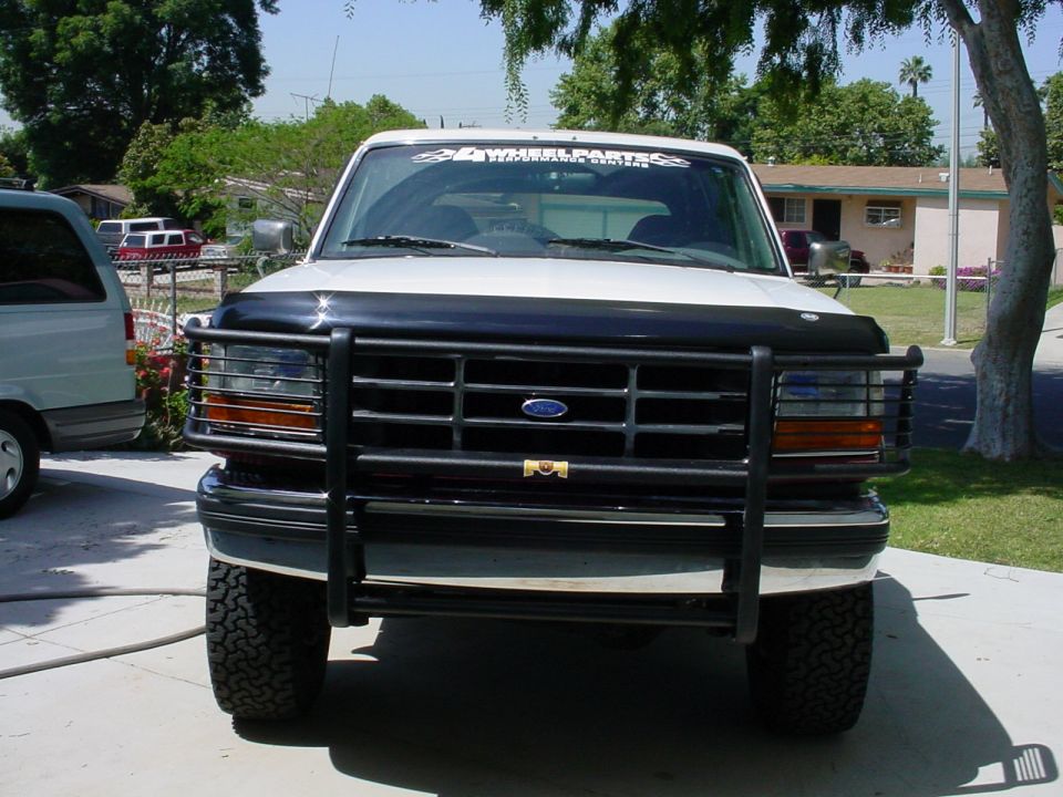 White Ford Bronco with black grille guard and "4 WHEEL PARTS" windshield banner