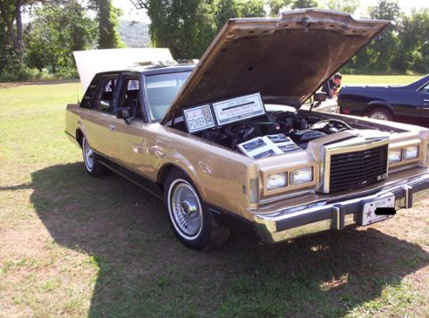 1991 Ford Crown Victoria LTD - A gold 1985 Lincoln Town Car is displayed with its hood open, revealing the engine and a descriptive sign.