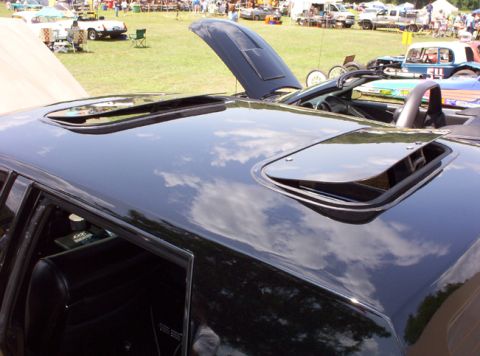 1991 Ford Crown Victoria LTD - Close-up of a car's roof showing two open sunroofs, with a crowd and other vehicles visible in the distance.