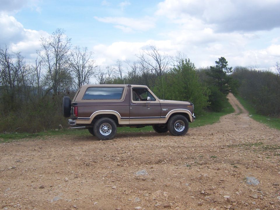 Brown Ford Bronco parked on a dirt road with trees and a cloudy sky