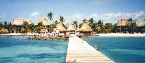 1996 Ford Bronco - Tropical resort with thatched-roof bungalows on a white sand beach, viewed from a wooden pier over turquoise water.