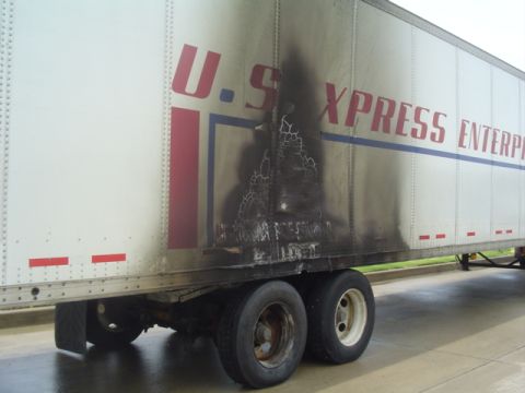 1996 Ford Crown Victoria - A trailer shows extensive fire damage on its side, obscuring some of the company's branding.