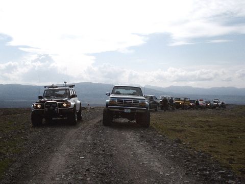 1996 Ford Bronco - A lifted 1996 Ford Bronco leads a convoy of off-road vehicles along a gravel path with mountains in the background.
