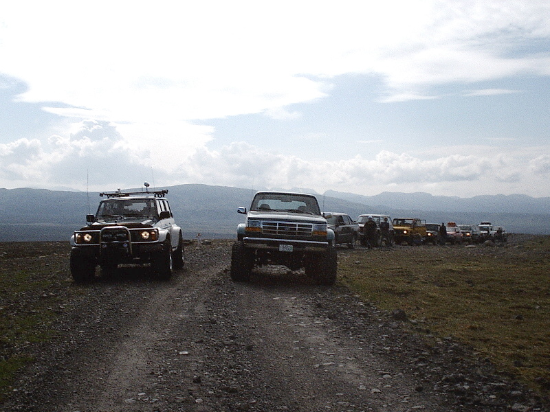 Row of lifted off-road trucks and SUVs on a gravel track in highland terrain