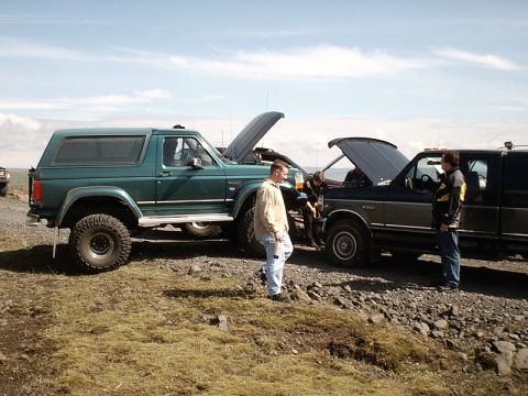 1996 Ford Bronco - Two trucks are parked on a gravelly area with people around them, one with its hood open.