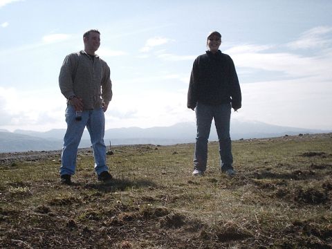 1996 Ford Bronco - Two people stand on a grassy hill under a cloudy sky with mountains in the background.