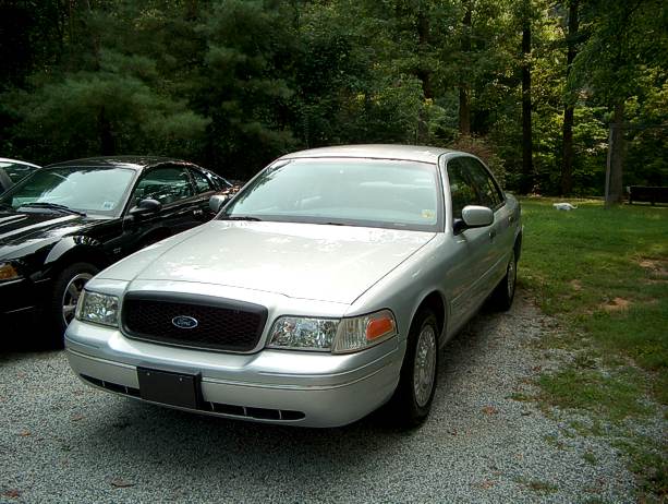 Silver Ford Crown Victoria sedan parked at the edge of a wooded yard