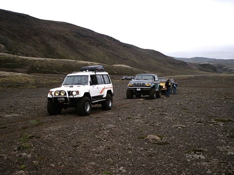1996 Ford Bronco - A convoy of off-road vehicles traverses a rocky, barren landscape under an overcast sky.