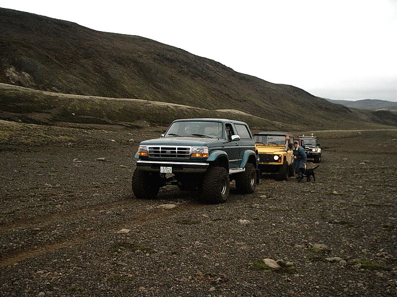 Lifted dark green Ford Bronco on gravel with other 4x4s in barren hills