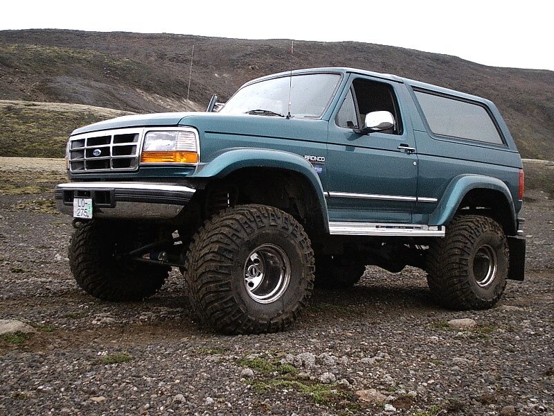Lifted teal Ford Bronco SUV on big mud tires parked on gravel in hilly terrain