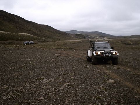 1996 Ford Bronco - Two off-road vehicles traverse a desolate, rocky terrain under an overcast sky.