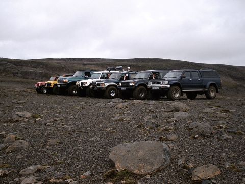 1996 Ford Bronco - A convoy of off-road vehicles is lined up on a rocky terrain under a cloudy sky.