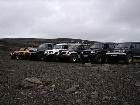 1996 Ford Bronco - Several off-road vehicles are lined up on a gravelly, desolate terrain.