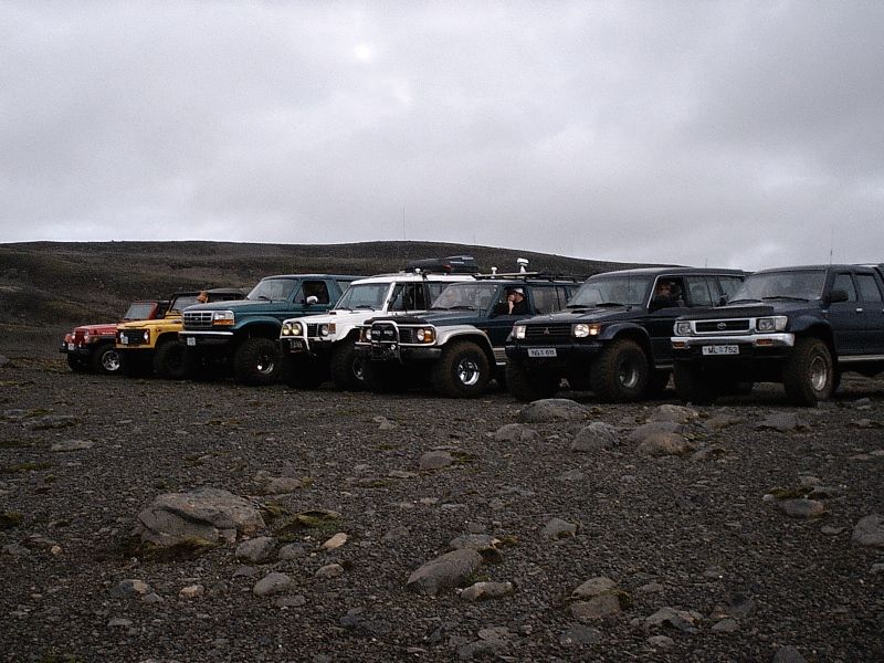 Row of lifted 4x4 SUVs on oversized tires parked on rocky terrain under gray sky