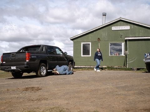 1996 Ford Bronco - A person works on a black Chevrolet Avalanche parked outside a green building.