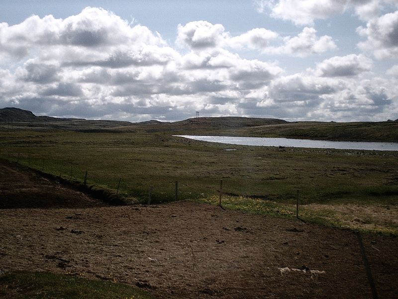 Barren grassy landscape with a pond and cloudy sky, no vehicle present