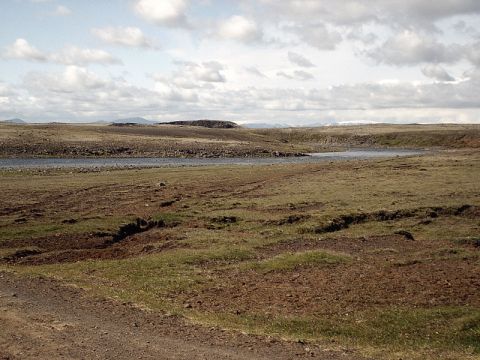 1996 Ford Bronco - A vast, undeveloped landscape features a winding river and rolling hills beneath a dramatic, cloud-filled sky.