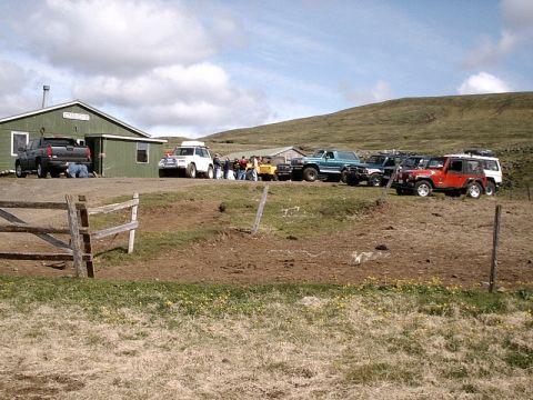 1996 Ford Bronco - A group of off-road vehicles are gathered near a building in a rural, hilly landscape.