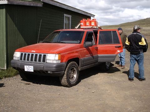 1996 Ford Bronco - A red Jeep Grand Cherokee is parked outside a building with its doors open and gas cans on the roof.