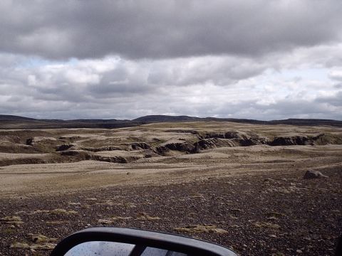 1996 Ford Bronco - A view from a vehicle's side mirror captures a vast, desolate landscape under a dramatic, cloudy sky.
