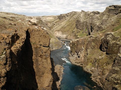 1996 Ford Bronco - A wide river carves its way through a deep, rocky canyon, with cliffs on either side and a cloudy sky overhead.