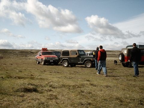 1996 Ford Bronco - A group of off-road vehicles are parked in a wide-open, grassy area with people milling about.