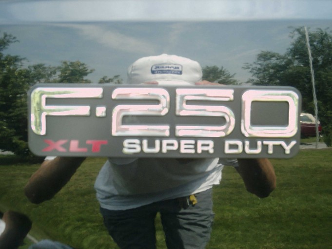 Chrome F-250 XLT Super Duty tailgate emblem held up by a person in a cap