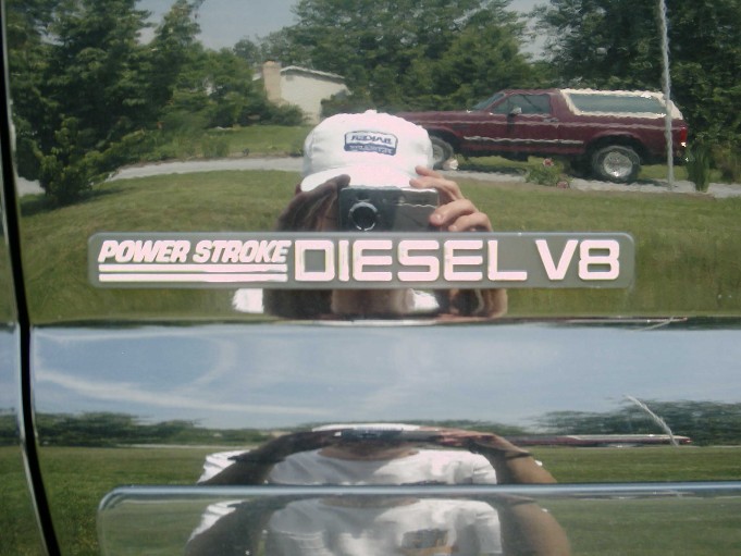Chrome Power Stroke Diesel V8 fender badge on black truck reflecting photographer and red SUV