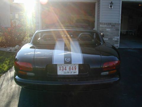 1996 Dodge Viper - Rear view of a black Dodge Viper with white racing stripes, parked in front of a garage.