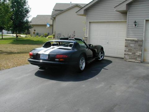 1996 Dodge Viper - Rear view of a black 1996 Dodge Viper with white stripes, parked in front of a suburban garage.