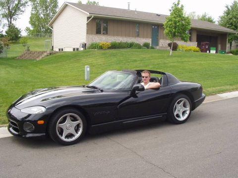 1996 Dodge Viper - A black 1996 Dodge Viper convertible is shown with a driver behind the wheel, parked on a suburban street.