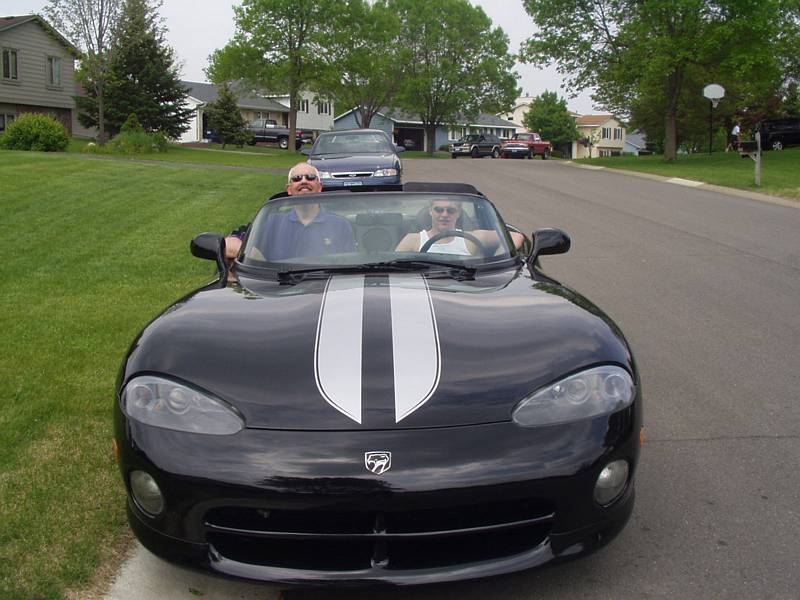 Black Dodge Viper convertible with silver stripes, front view, two people inside, on suburban street